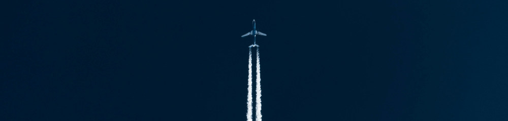 Photo of a commercial jet taken from the ground moving in the direction of the top of the page, on a dark blue sky with white contrails.